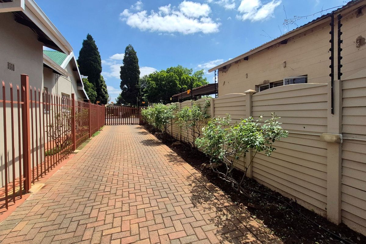 A paved side access path featuring metal security fencing, a precast concrete boundary wall with electric fencing, and a secure metal gate.
