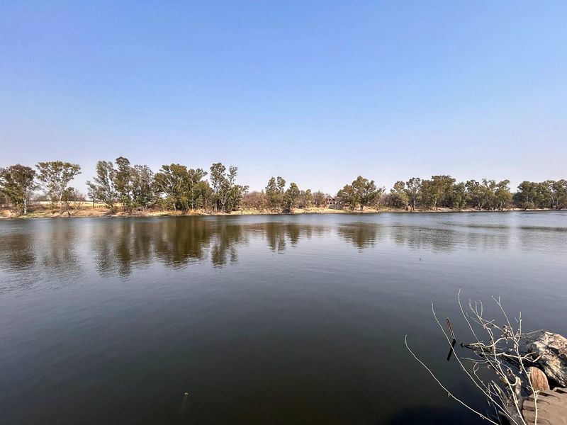 A scenic view of the river frontage featuring mature trees along the bank, highlighting the natural landscape and water access of the small holding.