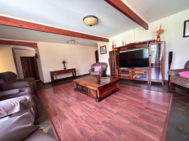 Spacious living room featuring a combination of slate and laminate wood flooring, accented by exposed timber ceiling beams.