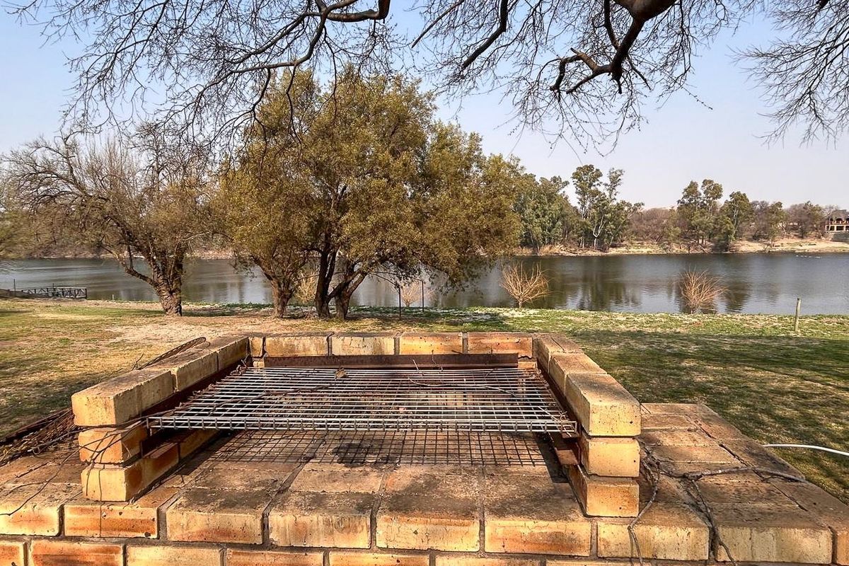 Outdoor brick braai area situated on a riverfront property, offering scenic water views and a natural landscape setting.
