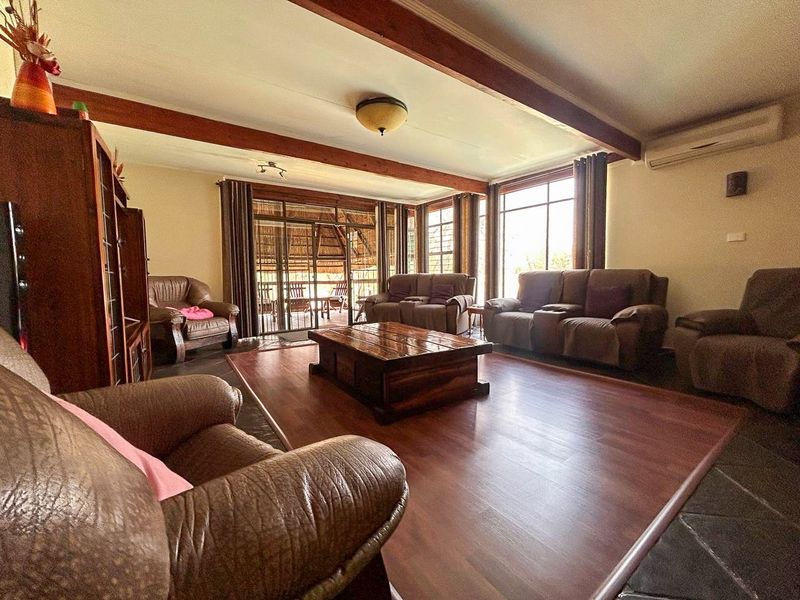 Spacious living room featuring exposed timber ceiling beams, laminate flooring, and large windows providing natural light and access to the outdoor patio area.