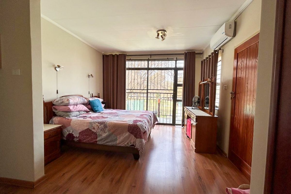 Spacious bedroom featuring laminate flooring, an air conditioning unit, and a sliding glass door with security gate providing access to the exterior.
