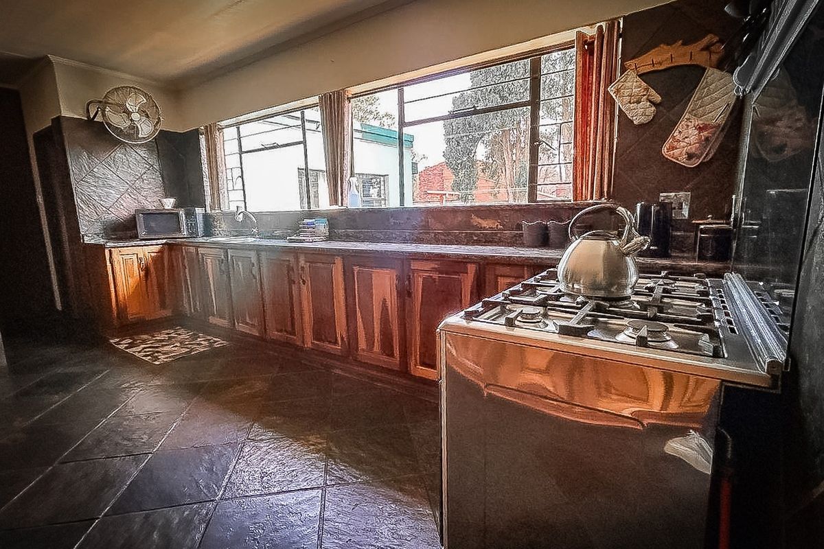 A functional kitchen featuring wooden cabinetry, a gas stove, and dark tiled flooring with ample natural light from a large window.