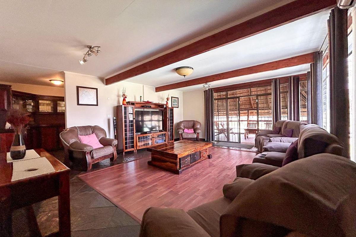 Spacious living room featuring exposed timber ceiling beams, a mix of slate and laminate flooring, and sliding glass doors leading to an outdoor area.