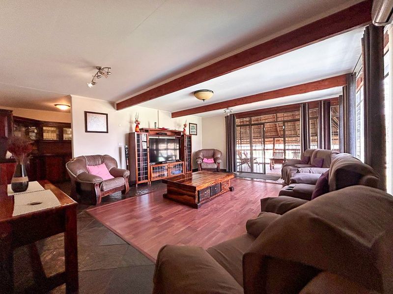 Spacious living room featuring exposed timber ceiling beams, a mix of slate and laminate flooring, and sliding glass doors leading to an outdoor area.
