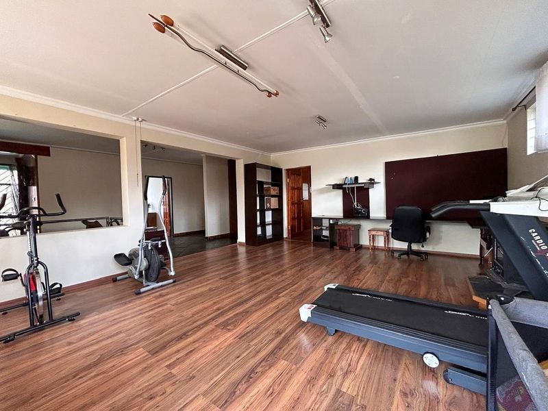 A spacious room currently utilized as a home gym, featuring durable laminate flooring, a built-in desk area, and neutral wall finishes.