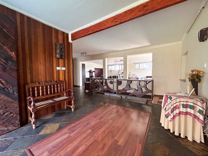 Spacious open-plan living area featuring rustic slate tile flooring, warm timber wall paneling, and a decorative metal partition separating the living and gym spaces.