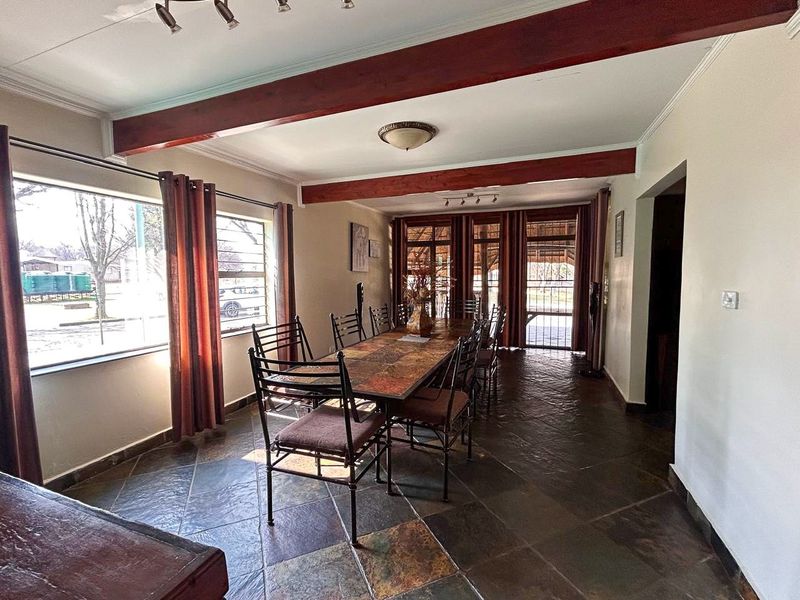 Spacious dining room featuring rustic slate tile flooring, exposed timber ceiling beams, and large windows providing ample natural light.