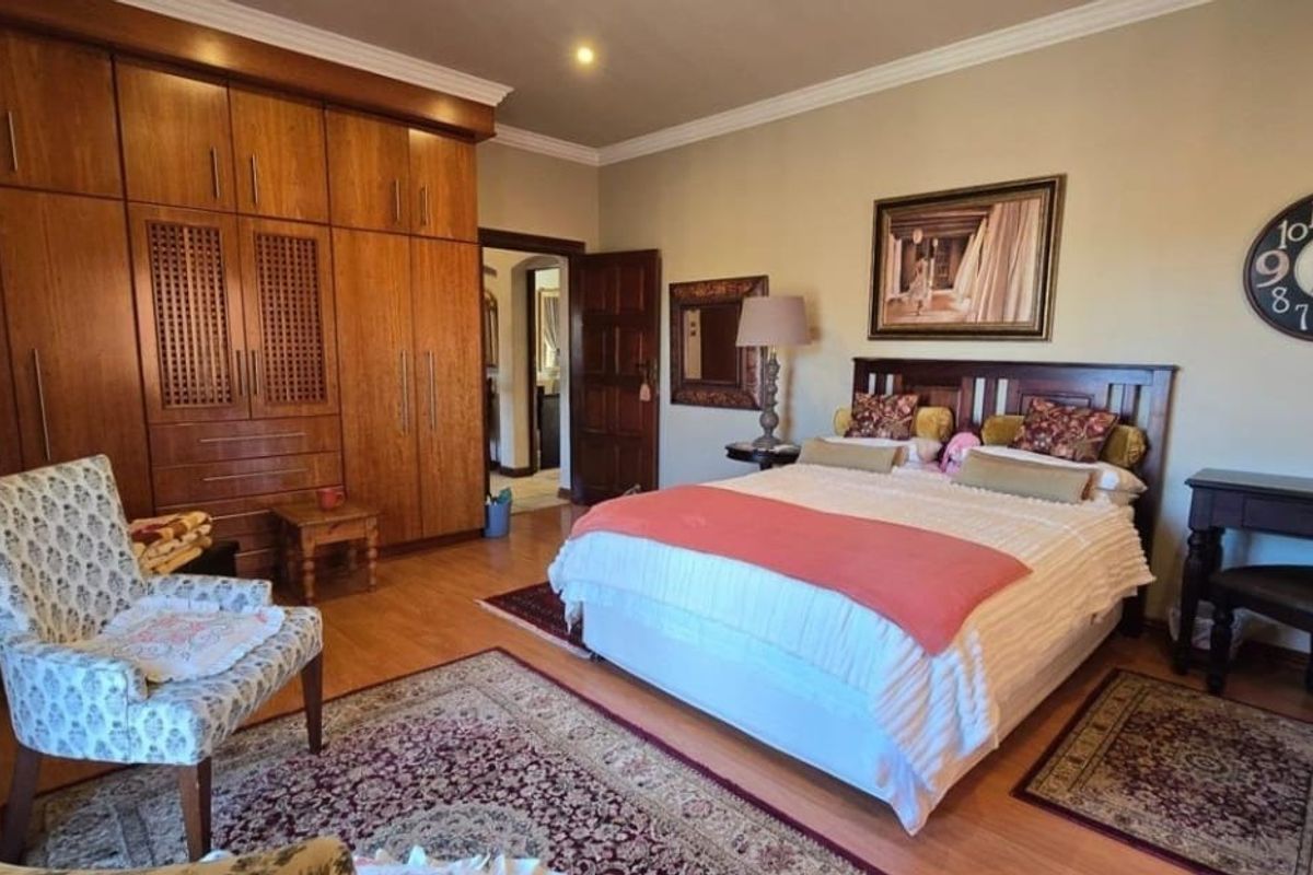 Spacious bedroom featuring extensive built-in wooden cabinetry, laminate flooring, and classic cove cornicing, offering ample storage and a warm, traditional aesthetic.