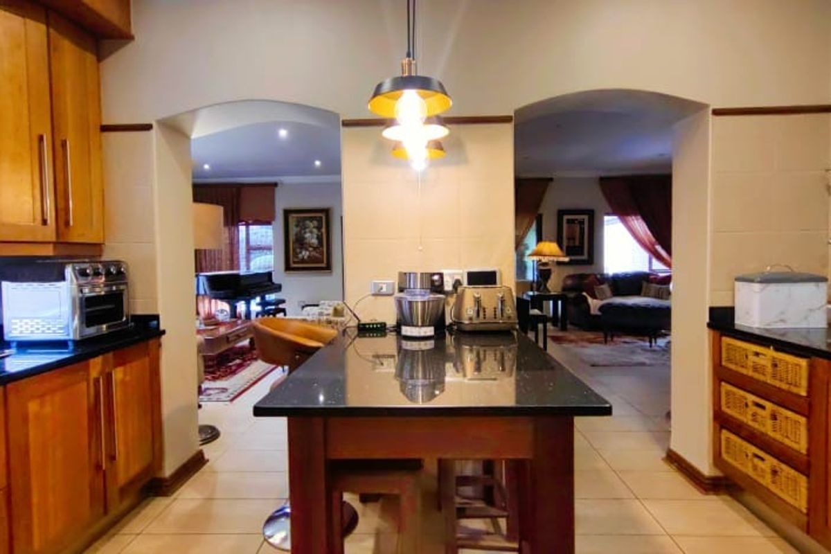 A well-maintained kitchen featuring warm wooden cabinetry, granite countertops, and a central island, with open-plan access to the adjacent living areas.