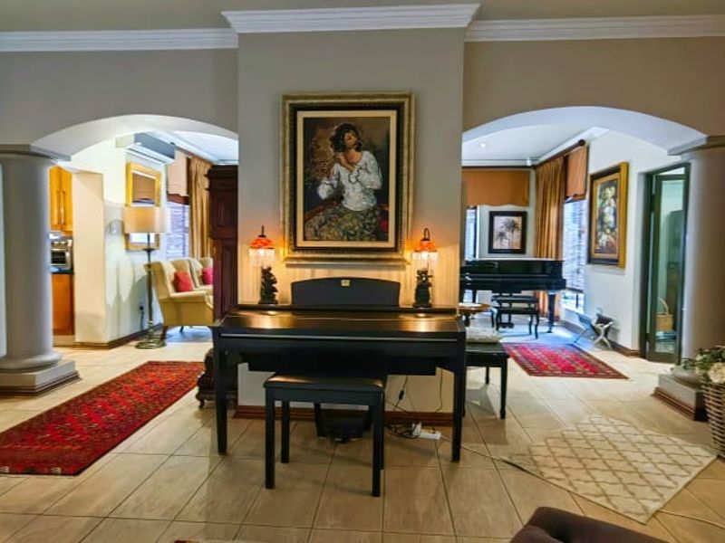 Spacious open-plan living area featuring elegant architectural archways, decorative columns, crown molding, and neutral tiled flooring throughout the connected spaces.