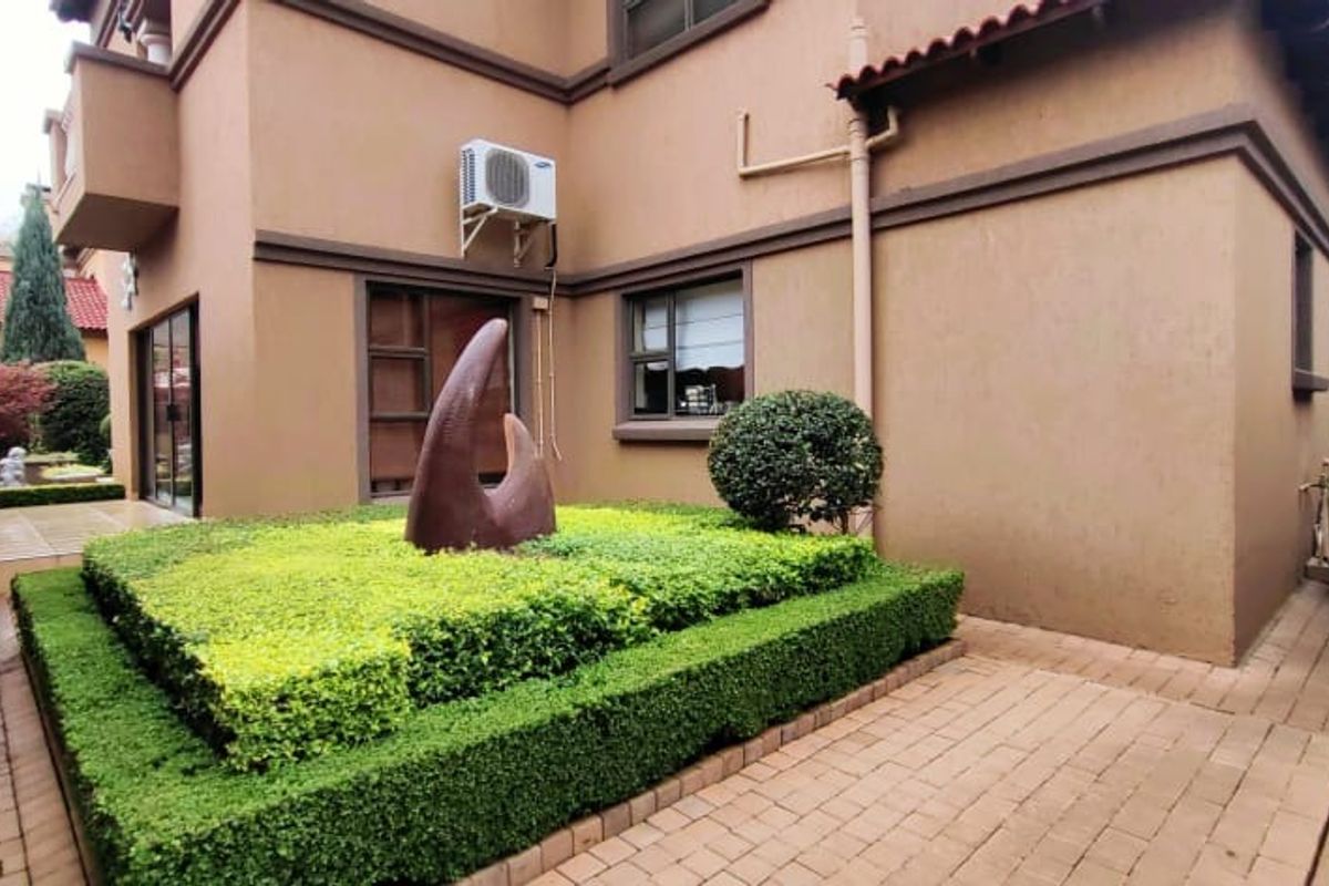 A well-maintained rear exterior view featuring paved walkways, a landscaped garden bed, and a tidy building facade with an installed air conditioning unit.