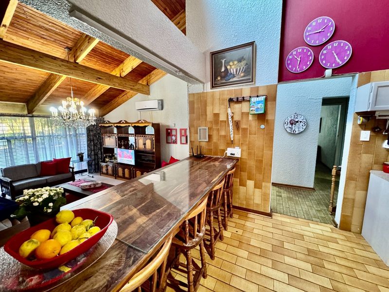 Open-plan living area featuring exposed timber ceiling beams, a tiled breakfast bar, and ceramic wall finishes, offering a spacious and functional layout.