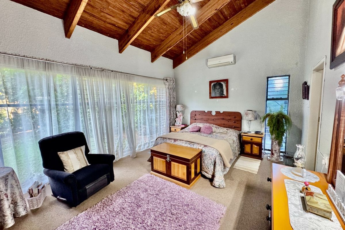 Spacious bedroom featuring a high vaulted timber ceiling with exposed beams, split-system air conditioning, and large sliding glass doors providing garden access.