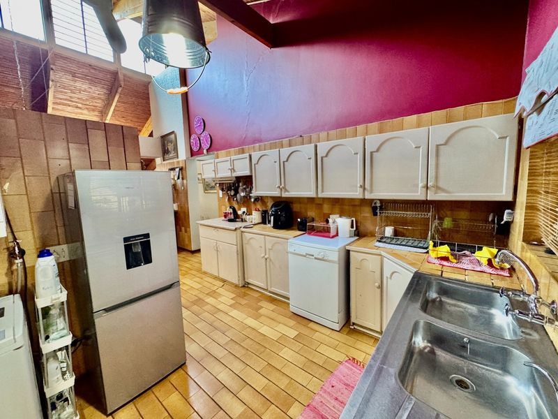 A dated kitchen featuring built-in cabinetry, a double basin stainless steel sink, tiled backsplash, and exposed timber ceiling beams.