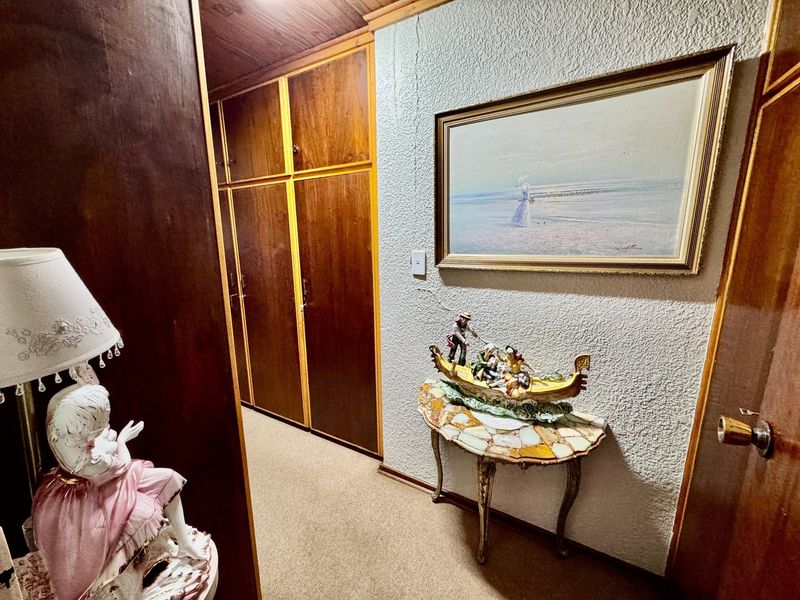 A hallway featuring built-in wooden cabinetry, textured walls, and a timber ceiling, showing signs of wear including a visible wall crack.