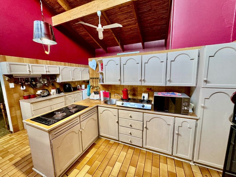 A rustic kitchen featuring exposed timber beams, tiled flooring, and extensive built-in cabinetry with integrated cooktops and prep areas.