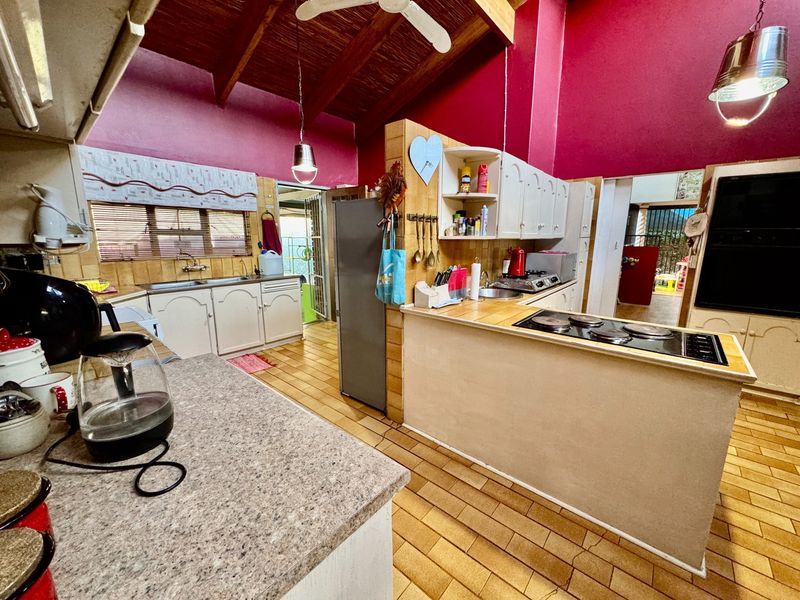 Spacious kitchen featuring exposed timber ceiling beams, tiled countertops, built-in cabinetry, and an electric hob, offering a functional layout with potential for modernization.