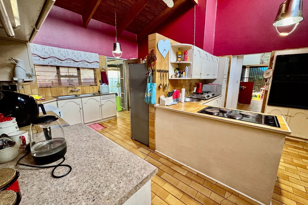 Spacious kitchen featuring exposed timber ceiling beams, tiled countertops, built-in cabinetry, and an electric hob, offering a functional layout with potential for modernization.