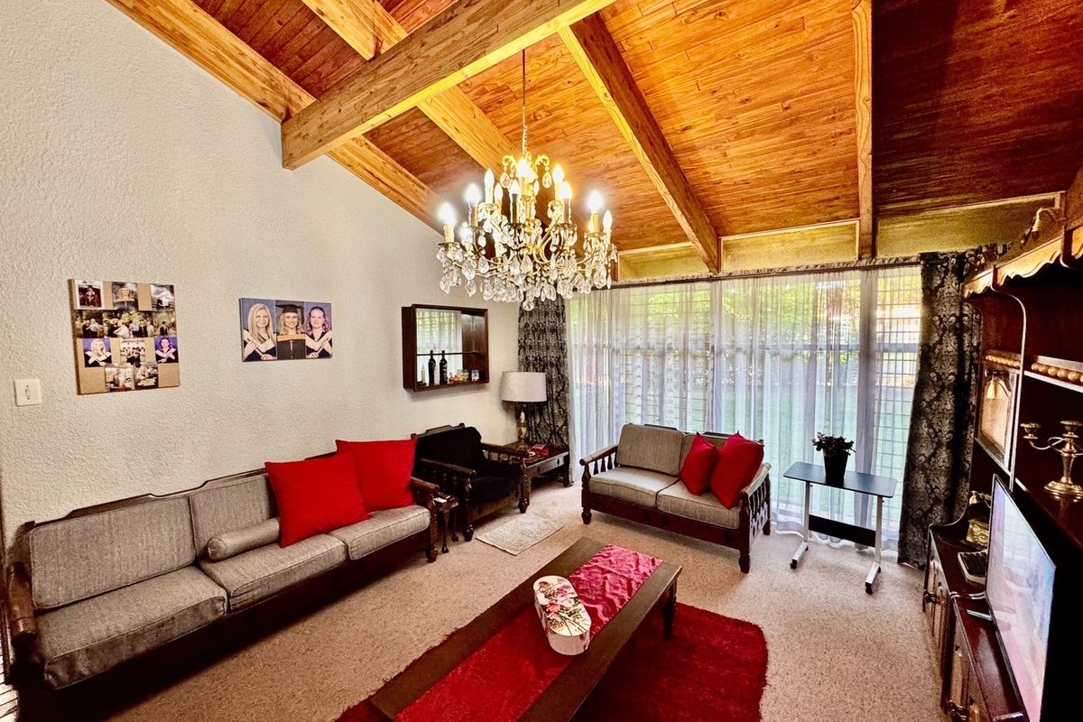 Spacious living room featuring a high vaulted timber ceiling with exposed beams, a classic crystal chandelier, and large windows providing natural light.