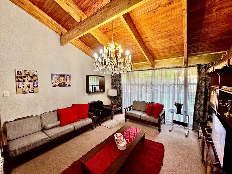 Spacious living room featuring a high vaulted timber ceiling with exposed beams, a classic crystal chandelier, and large windows providing natural light.