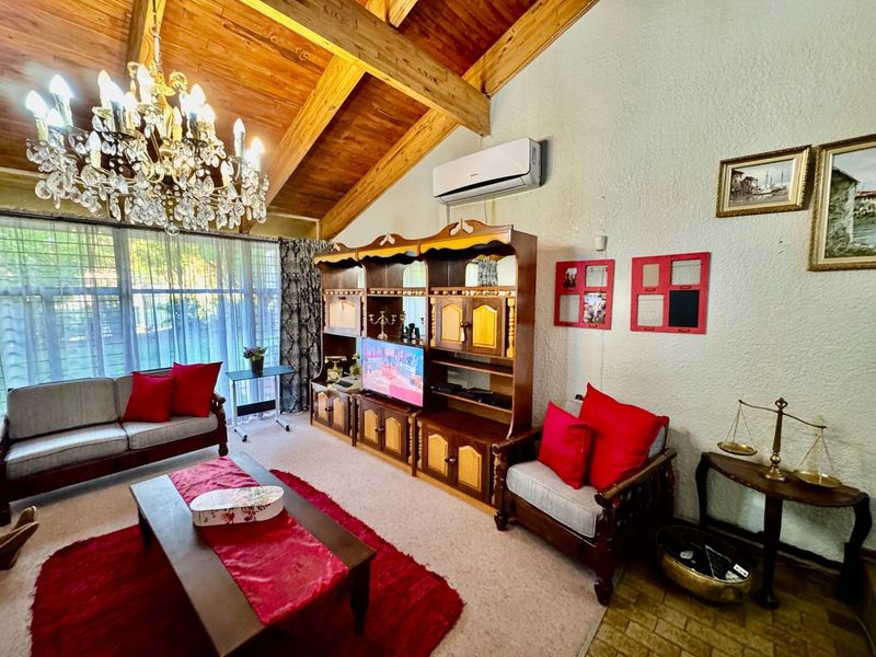 Spacious living room featuring a high exposed timber vaulted ceiling, large windows for natural light, and a wall-mounted split-system air conditioner.