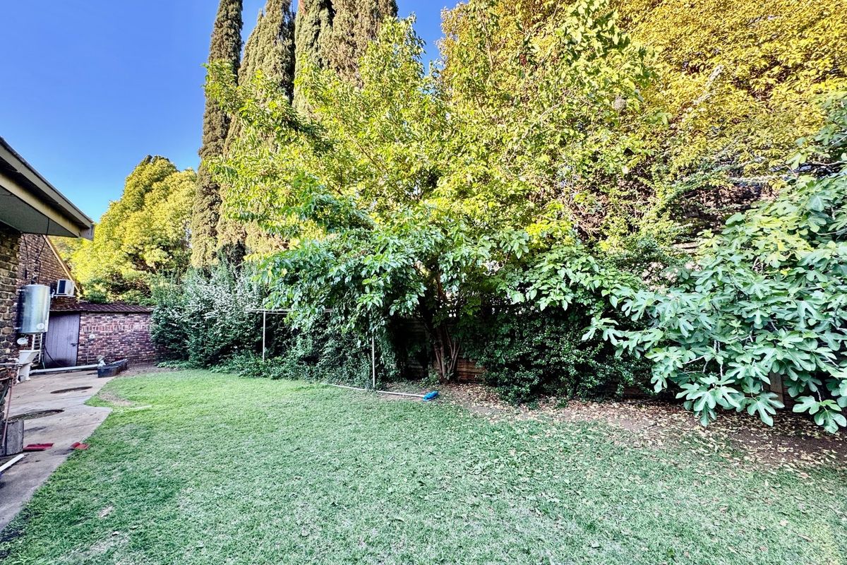 A private rear garden featuring a lawn, mature trees, established shrubbery, and a paved area with a wall-mounted geyser.