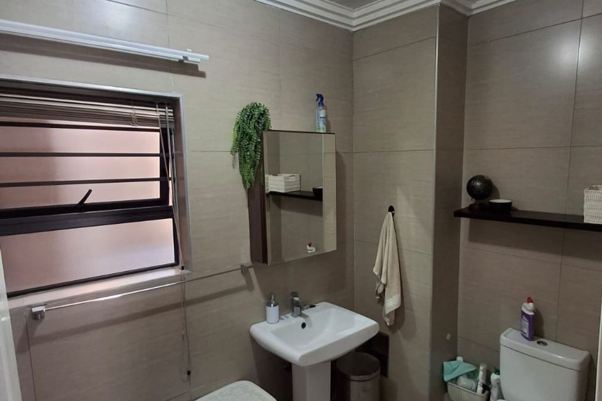 A functional bathroom featuring a pedestal washbasin, toilet, and neutral wall tiling. The space includes a medicine cabinet and window with security bars.