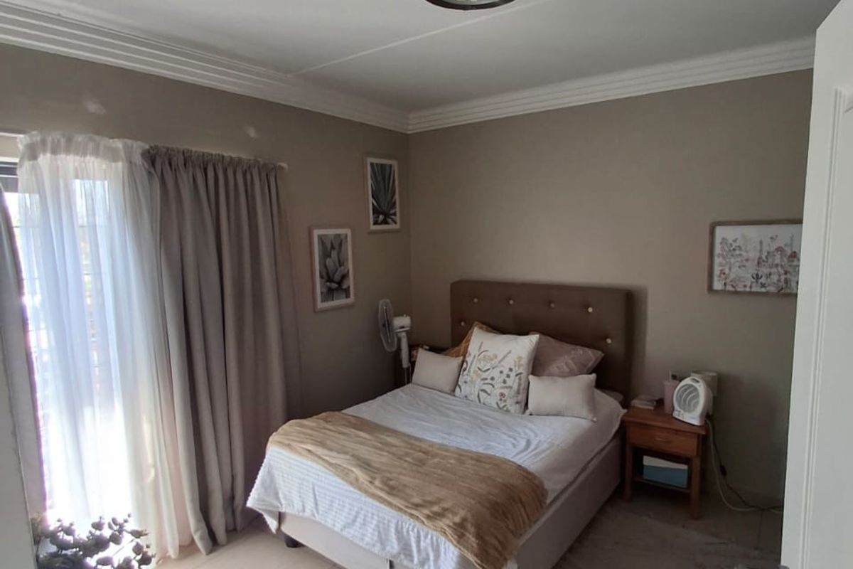 A well-maintained bedroom featuring neutral wall tones, tiled flooring, decorative ceiling cornicing, and a sliding door providing access to the exterior.
