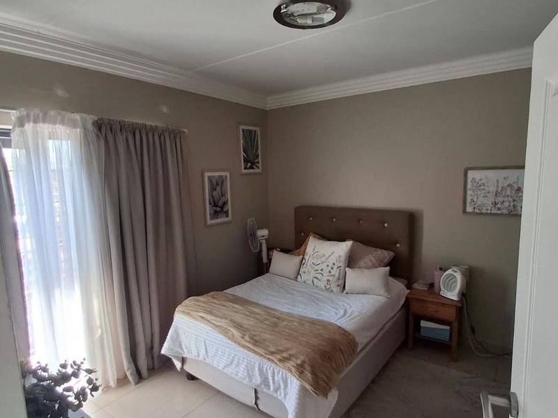 A well-maintained bedroom featuring neutral wall tones, tiled flooring, decorative ceiling cornicing, and a sliding door providing access to the exterior.