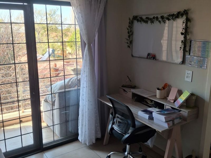 A functional home office space featuring tiled flooring, neutral walls, and a large sliding glass door providing access to a balcony.