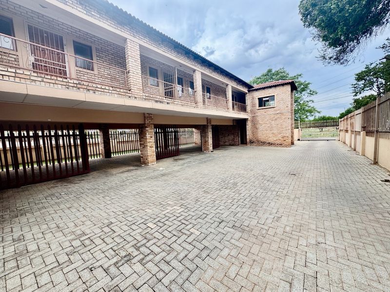 Exterior view of an apartment complex featuring a brick facade, paved driveway, and covered parking area with security gates.