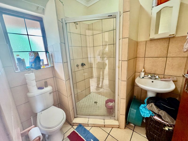 A functional bathroom featuring a shower enclosure, pedestal basin, and toilet with tiled finishes throughout.