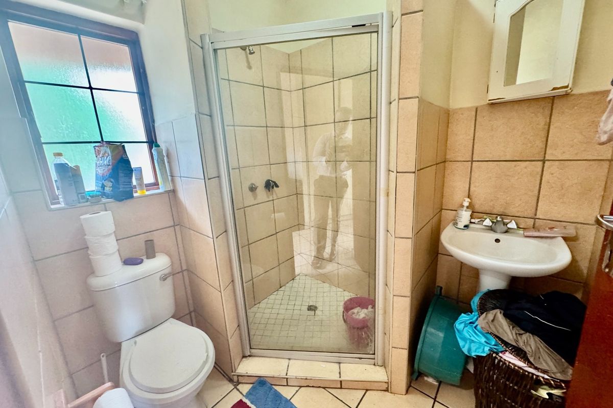 A functional bathroom featuring a shower enclosure, pedestal basin, and toilet with tiled finishes throughout.