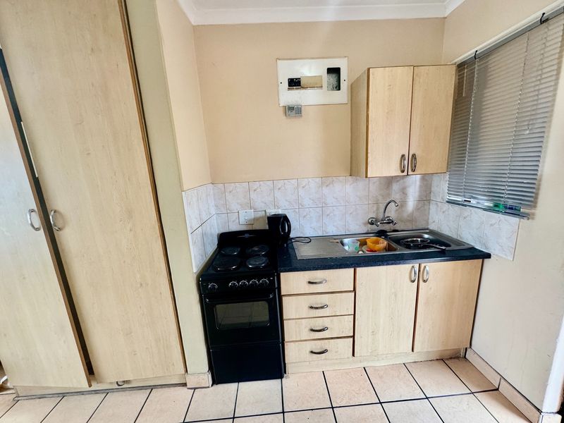 Compact kitchen featuring light wood-look cabinetry, laminate countertops, a stainless steel sink, and tiled backsplash, providing a functional and efficient cooking space.
