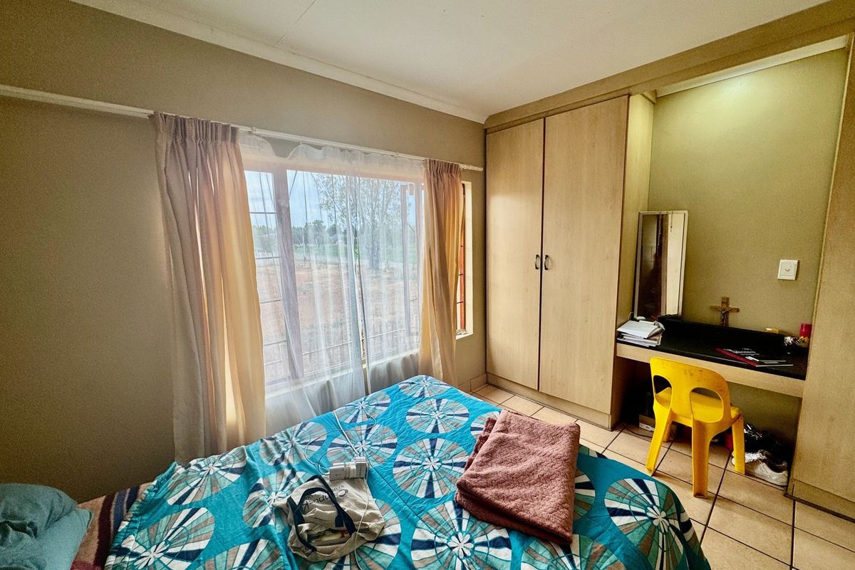 A functional bedroom featuring built-in cabinetry, a vanity area, tiled flooring, and a window with security bars.