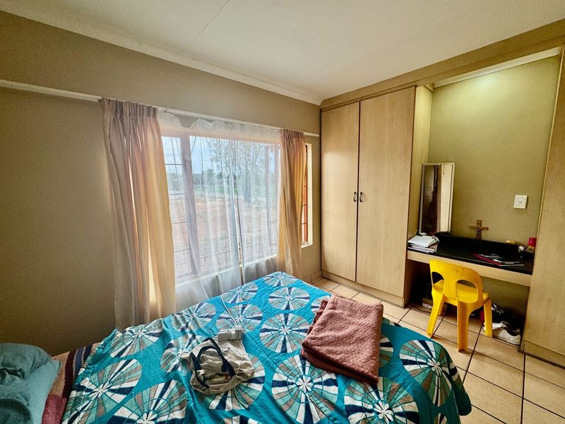 A functional bedroom featuring built-in cabinetry, a vanity area, tiled flooring, and a window with security bars.