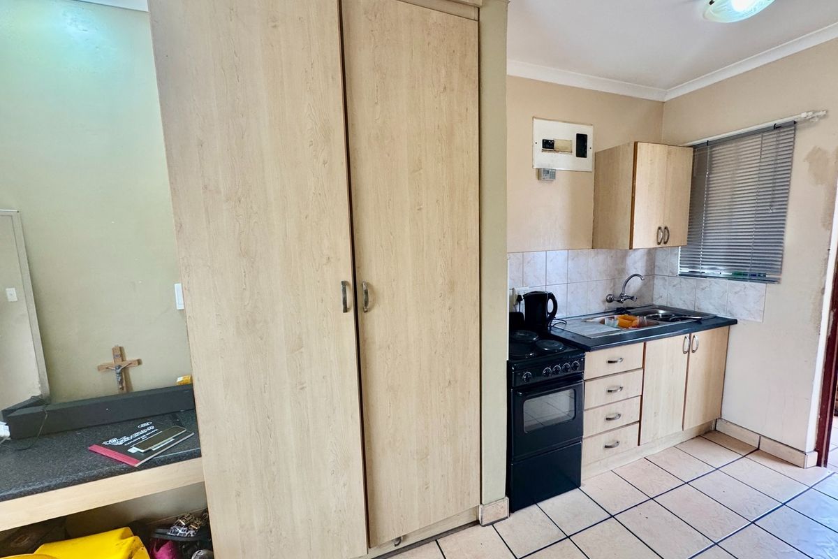 Compact kitchen featuring light wood-finish cabinetry, a freestanding stove, stainless steel sink, tiled backsplash, and tiled flooring.