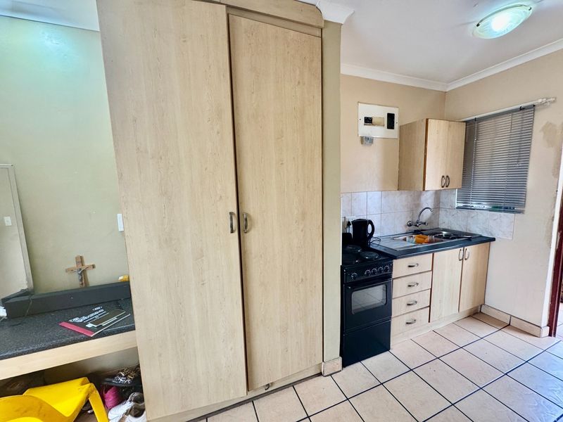 Compact kitchen featuring light wood-finish cabinetry, a freestanding stove, stainless steel sink, tiled backsplash, and tiled flooring.
