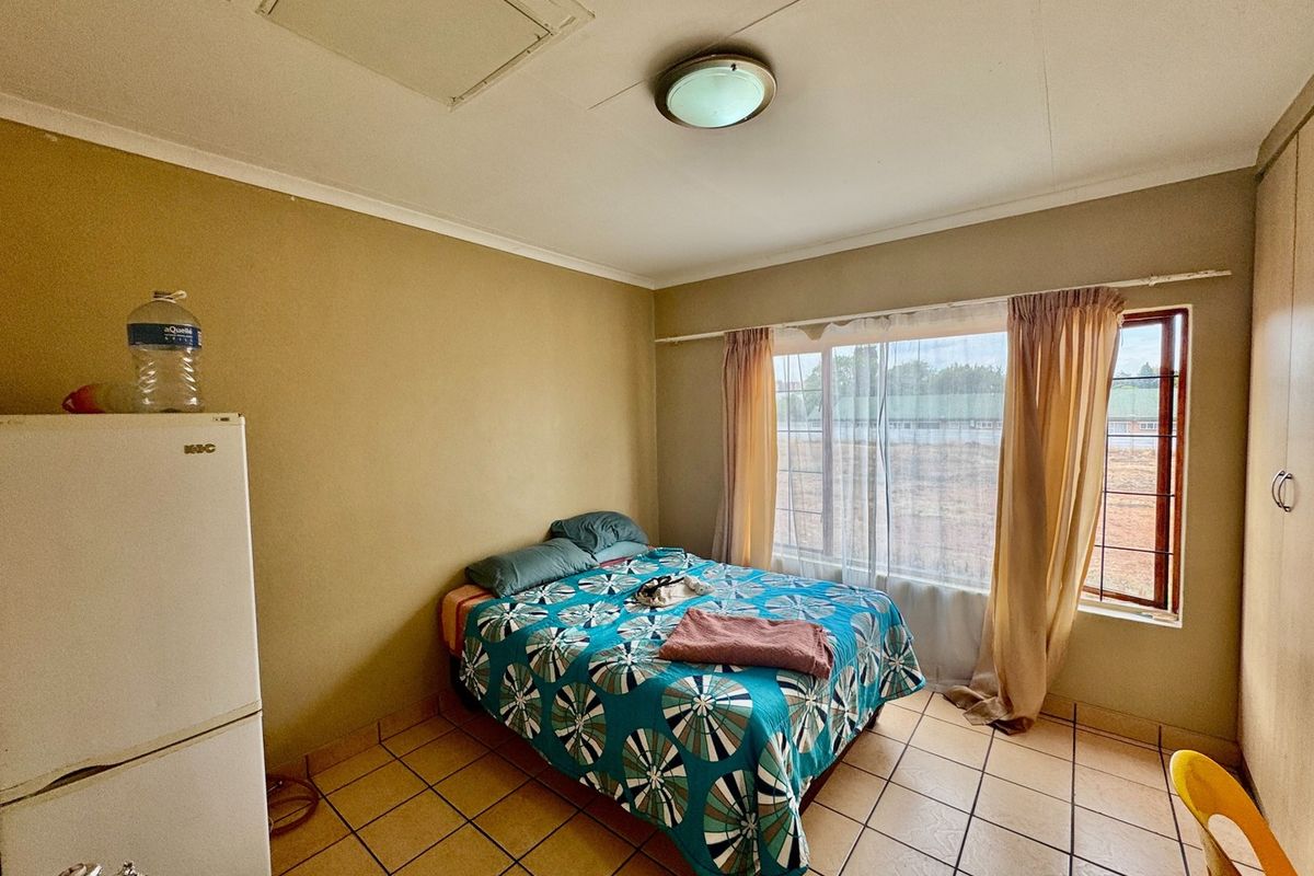 A bedroom featuring tiled flooring, built-in cupboards, and a large window, offering a functional space in need of cosmetic updates.
