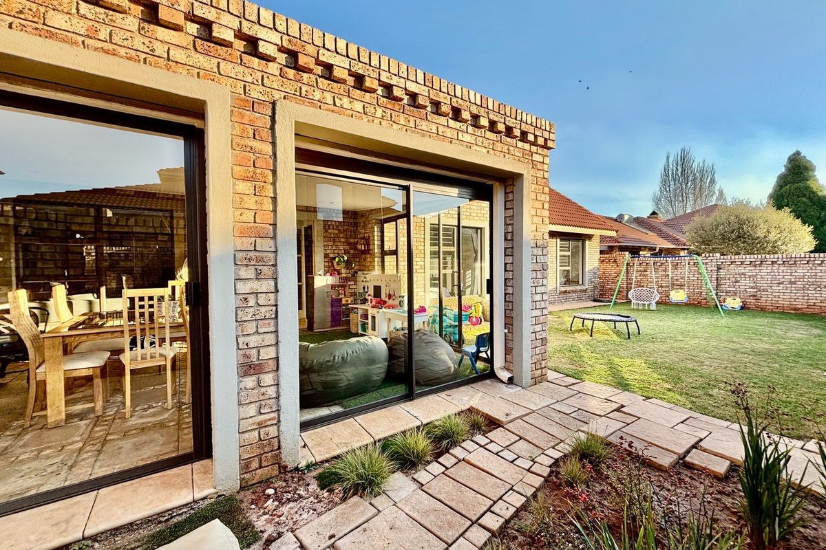 Rear view of the property featuring exposed brick architecture, large sliding glass doors, a paved garden path, and a well-maintained lawn.
