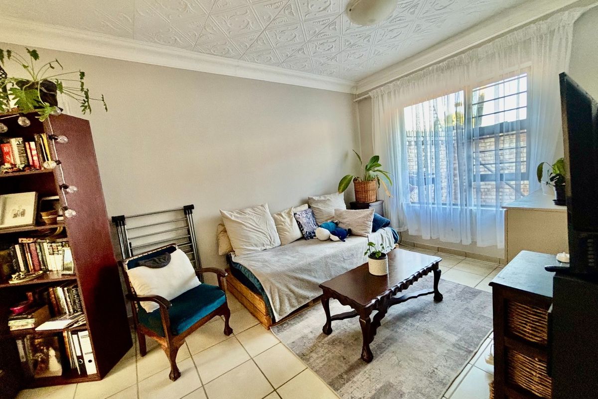 A living room featuring tiled flooring, decorative ceiling tiles, and a window fitted with security bars.