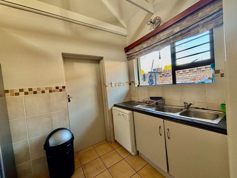 Functional scullery area featuring a double bowl stainless steel sink, tiled splashback, built-in cabinetry, and tiled flooring.