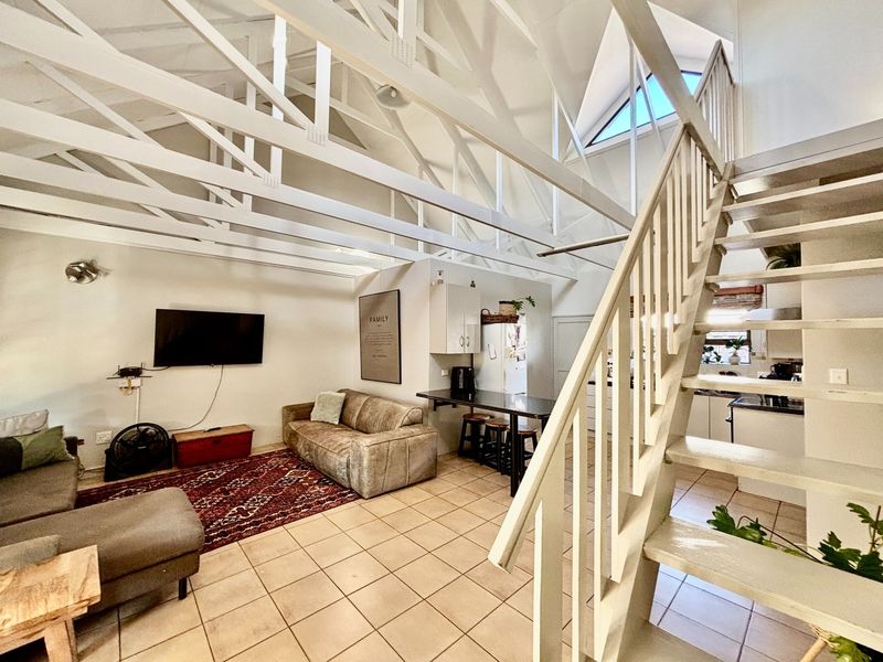 Open-plan living area featuring high vaulted ceilings with exposed timber trusses, a staircase to the upper level, and an integrated kitchen space.