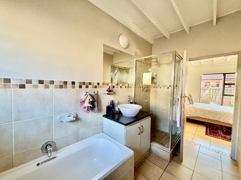 A functional bathroom featuring a built-in bathtub, a separate glass shower enclosure, and a vanity with a vessel sink, finished with neutral wall tiles.