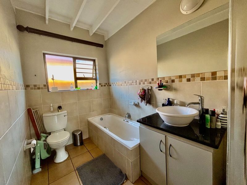 A functional bathroom featuring a built-in vanity with a vessel sink, a bathtub, and tiled wall finishes with exposed ceiling beams.
