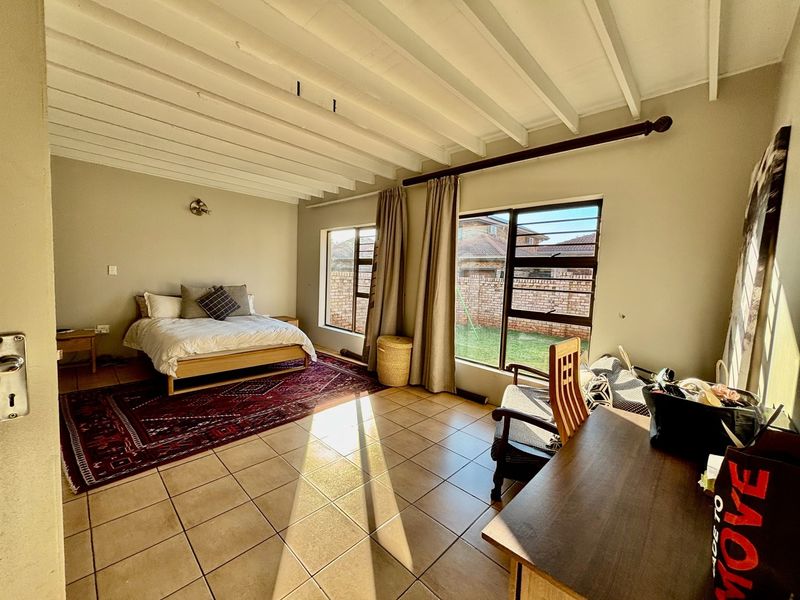 Spacious bedroom featuring tiled flooring, exposed beam ceilings, and large windows providing natural light and garden views.