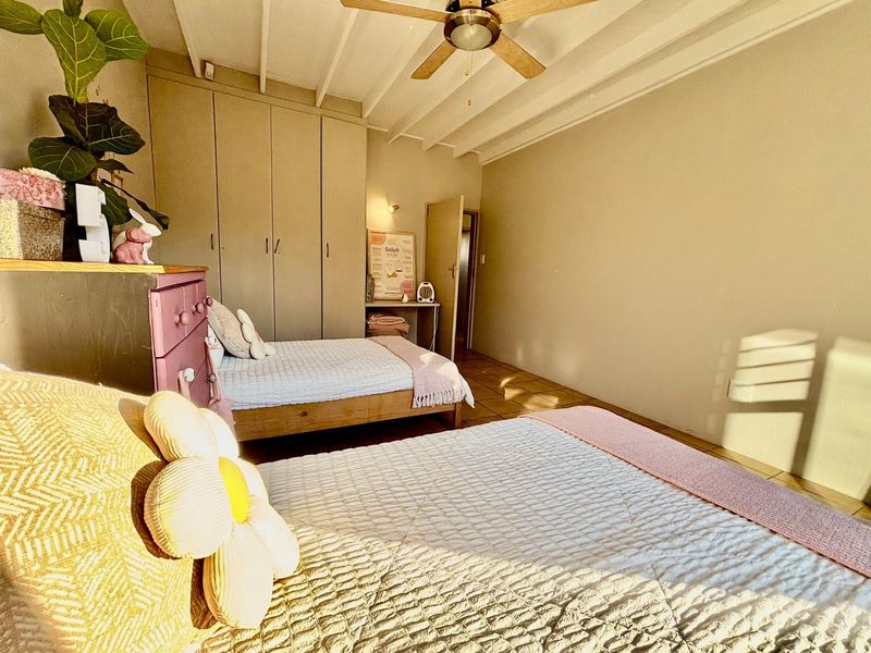 A bedroom featuring built-in cupboards, tiled flooring, and an exposed beam ceiling with a central ceiling fan.