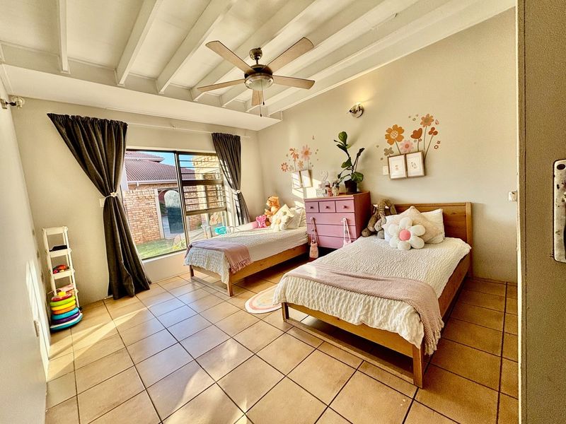 A bright bedroom featuring tiled flooring, an exposed beam ceiling with a central fan, and a sliding glass door providing natural light.