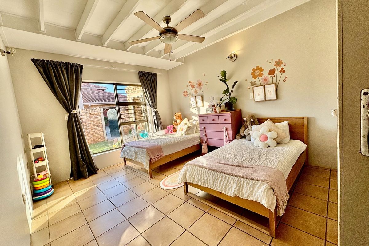 A bright bedroom featuring tiled flooring, an exposed beam ceiling with a central fan, and a sliding glass door providing natural light.